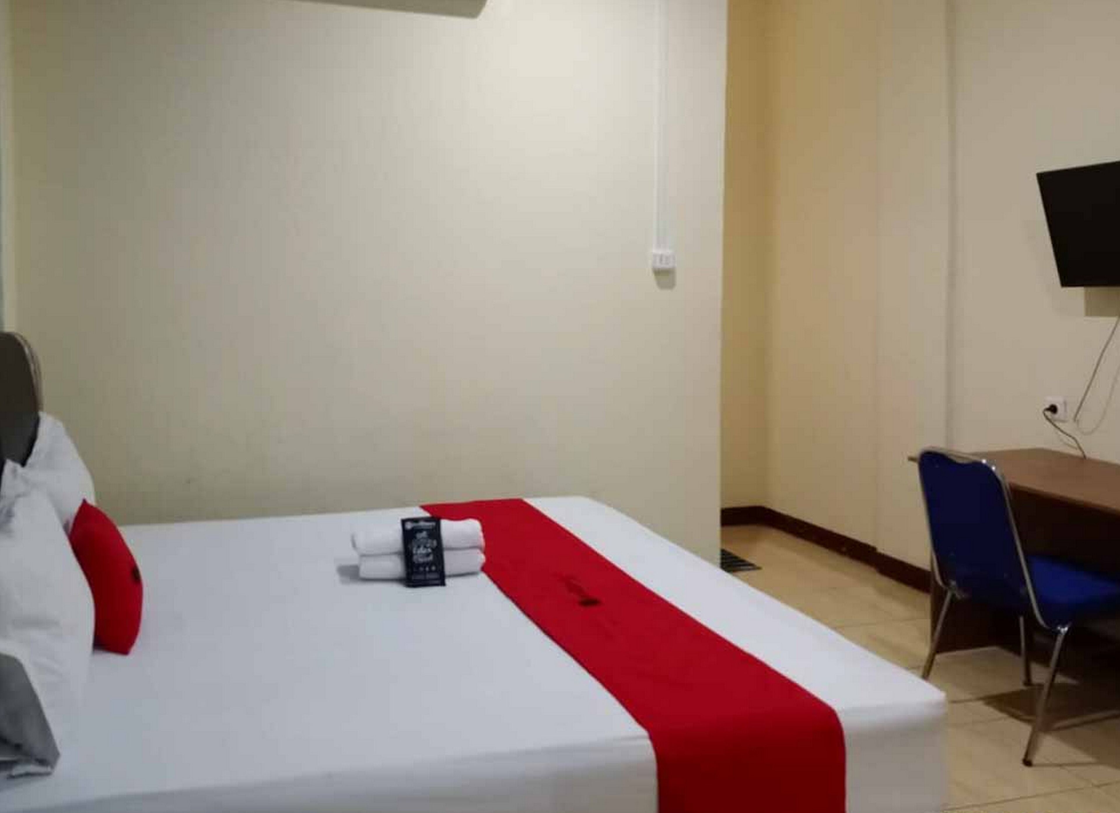 A hotel room with a bed, a desk, a chair, and a TV mounted on the wall.