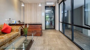 A modern reception area with a wooden reception desk, a glass coffee table, and a sofa with a red cushion. - RedDoorz Plus near Radio Dalam 3 (Jakarta)