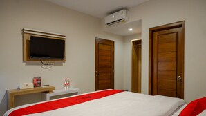 A hotel room with a bed, a TV mounted on the wall, a desk with a bottle, and two wooden doors. - RedDoorz near Sleman City Hall 2 (Ngaglik)