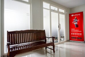 Un banco de madera en una habitación luminosa con ventanas grandes y un anuncio de RedDoorz.