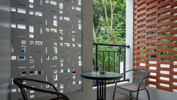 A balcony with a glass table and two wicker chairs, a white partition with cut-out windows, and a red wooden lattice. - RedDoorz near Sleman City Hall 2 (Ngaglik)