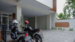 A motorcycle parked in a covered parking area with a brick wall and potted plants. - RedDoorz near Sleman City Hall 2 (Ngaglik)