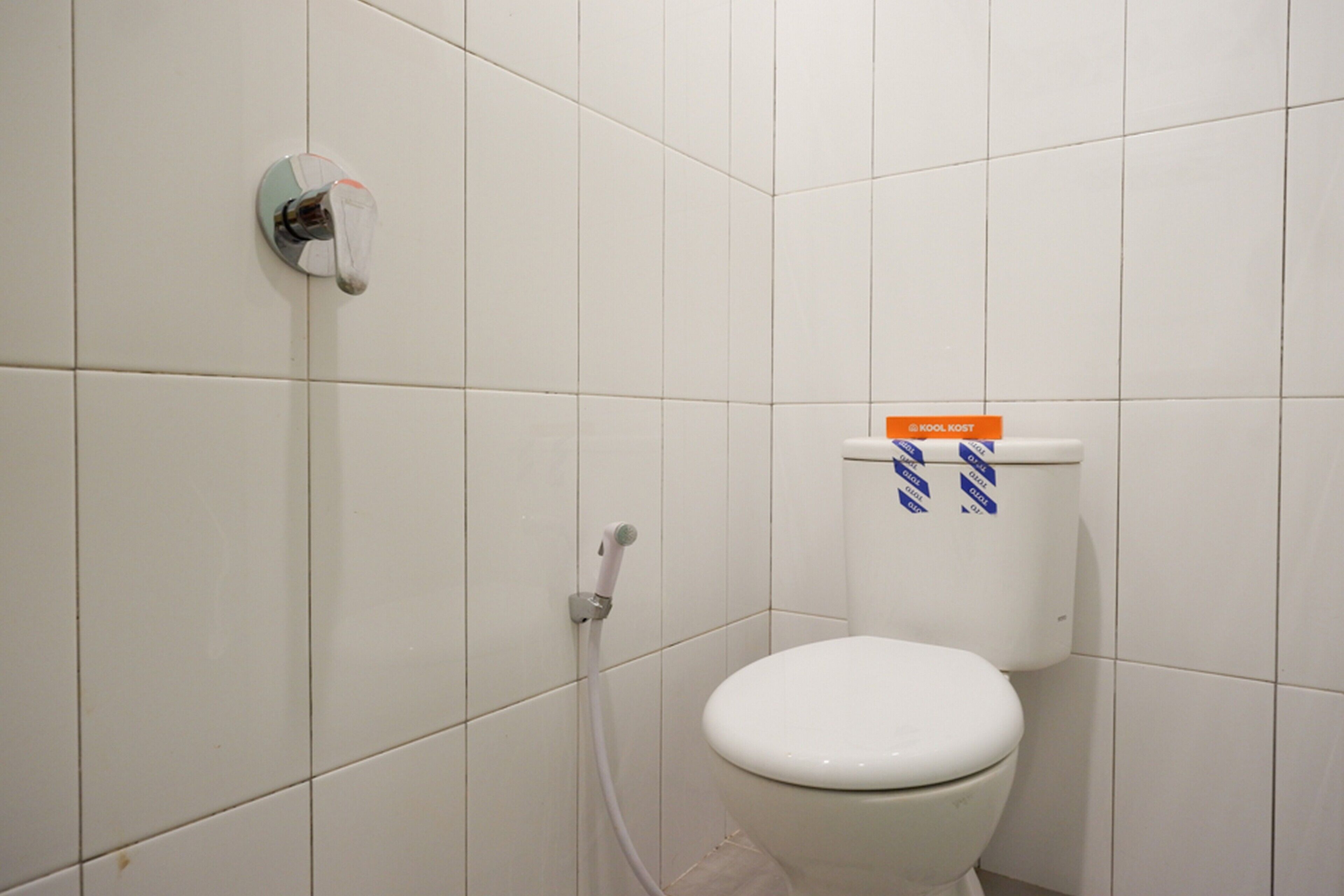 A white toilet with a blue and white striped label, a white wall, and a white floor.