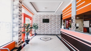 Un vestíbulo de hotel con un papel tapiz estampado, una recepción y plantas en macetas.