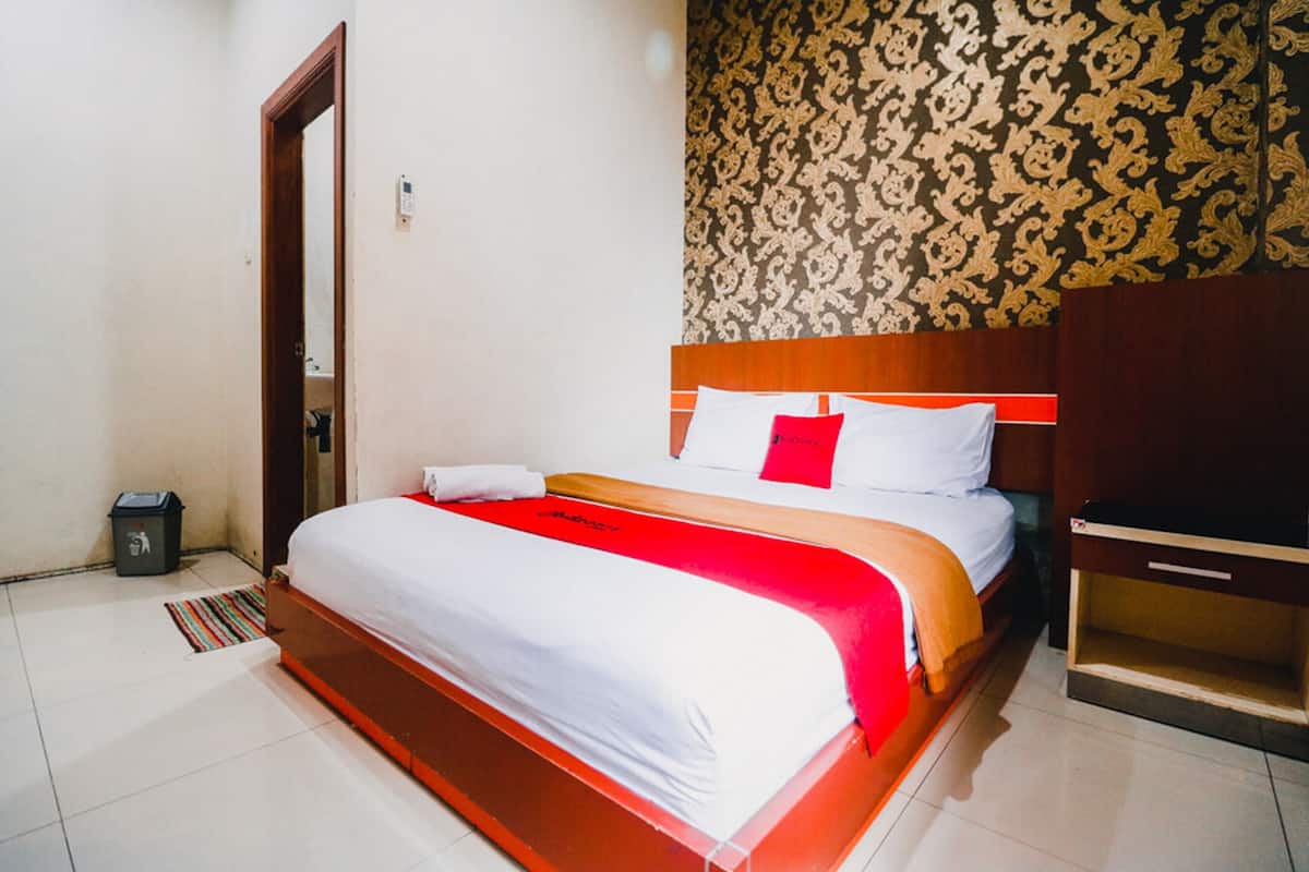 A neatly made bed with a red and white bedspread, a wooden headboard, and a nightstand with a drawer.