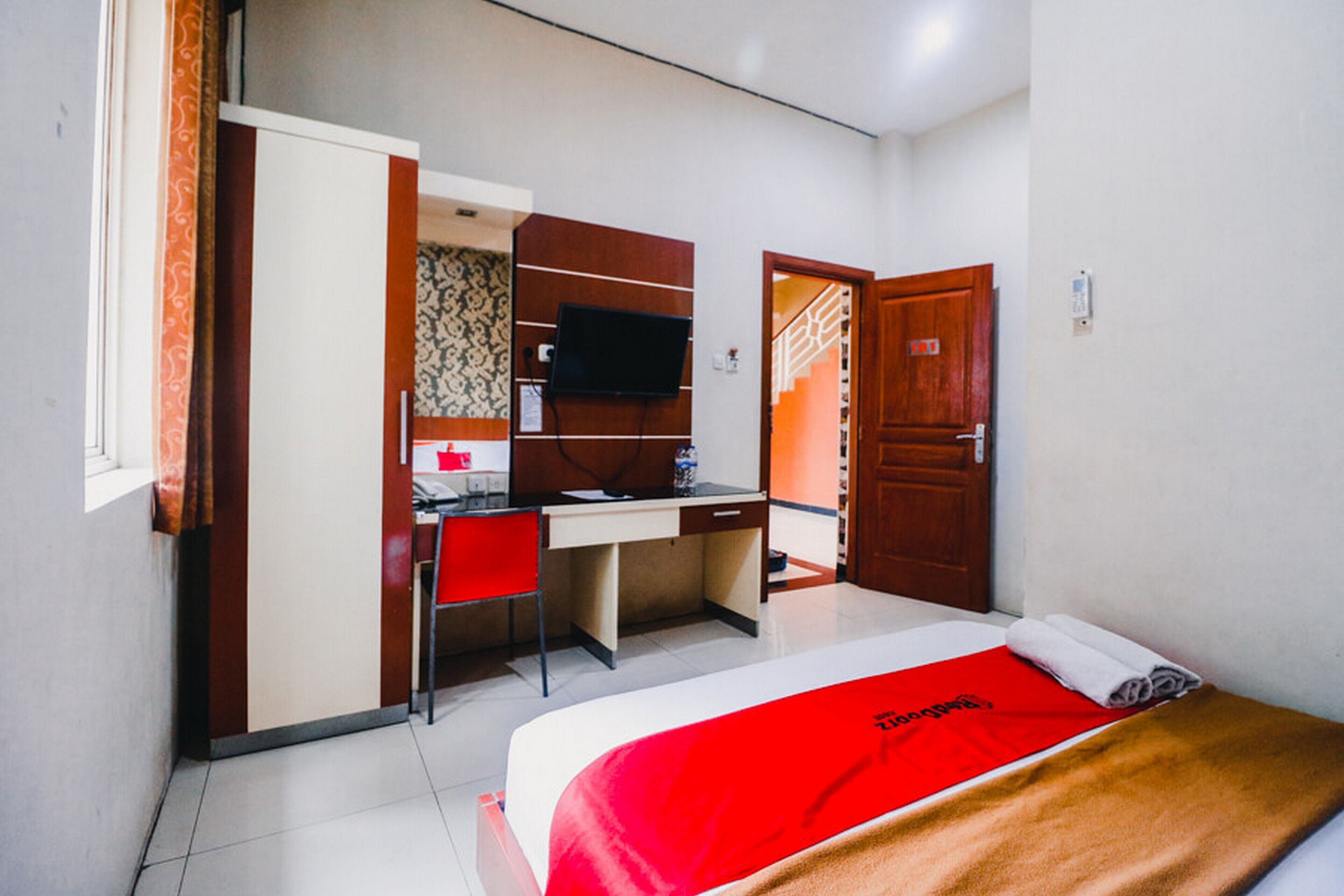 A hotel room with a bed, a desk, a chair, a television, and a wardrobe.