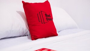 Een bed met witte lakens en een rode kussen met de tekst 'Red Door'.