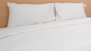 Een net opgemaakt bed met witte beddengoed en een houten hoofdeinde.