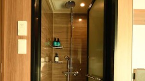 A narrow, enclosed shower area with a glass door, a showerhead, and a shelf with toiletries.