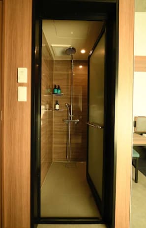 A narrow, enclosed shower area with a glass door, a showerhead, and a shelf with toiletries.