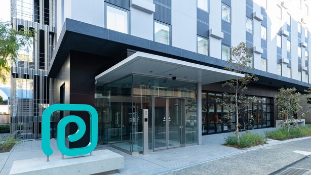 A modern building with a glass entrance and a teal logo.