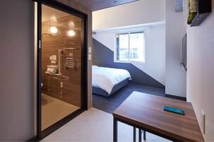 Una habitación de hotel moderna con cama, una mesita, una ventana y zona de ducha.