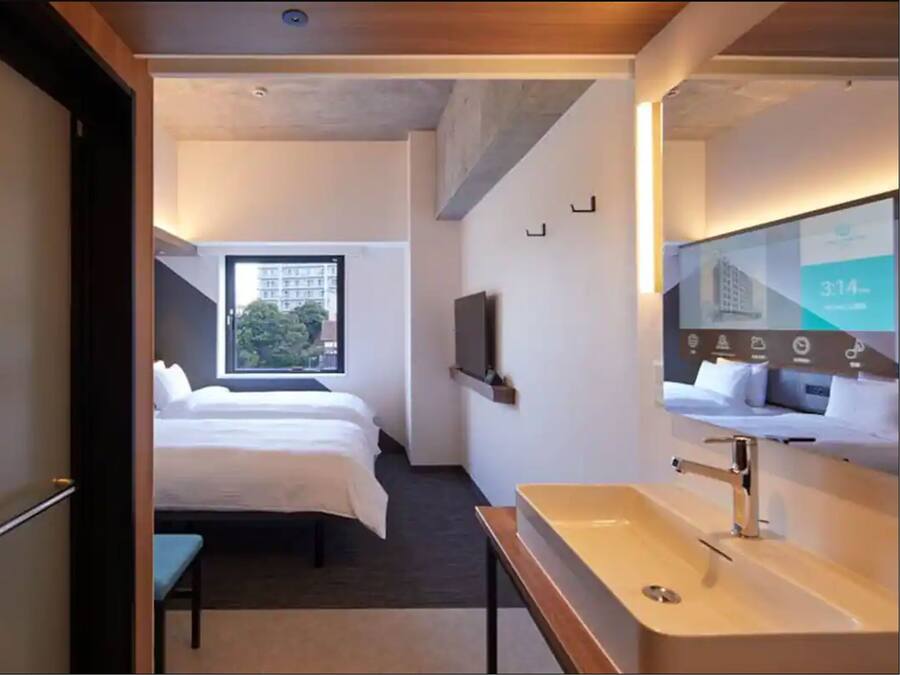 A hotel room with a bed, a bedside table, a large mirror, and a window.