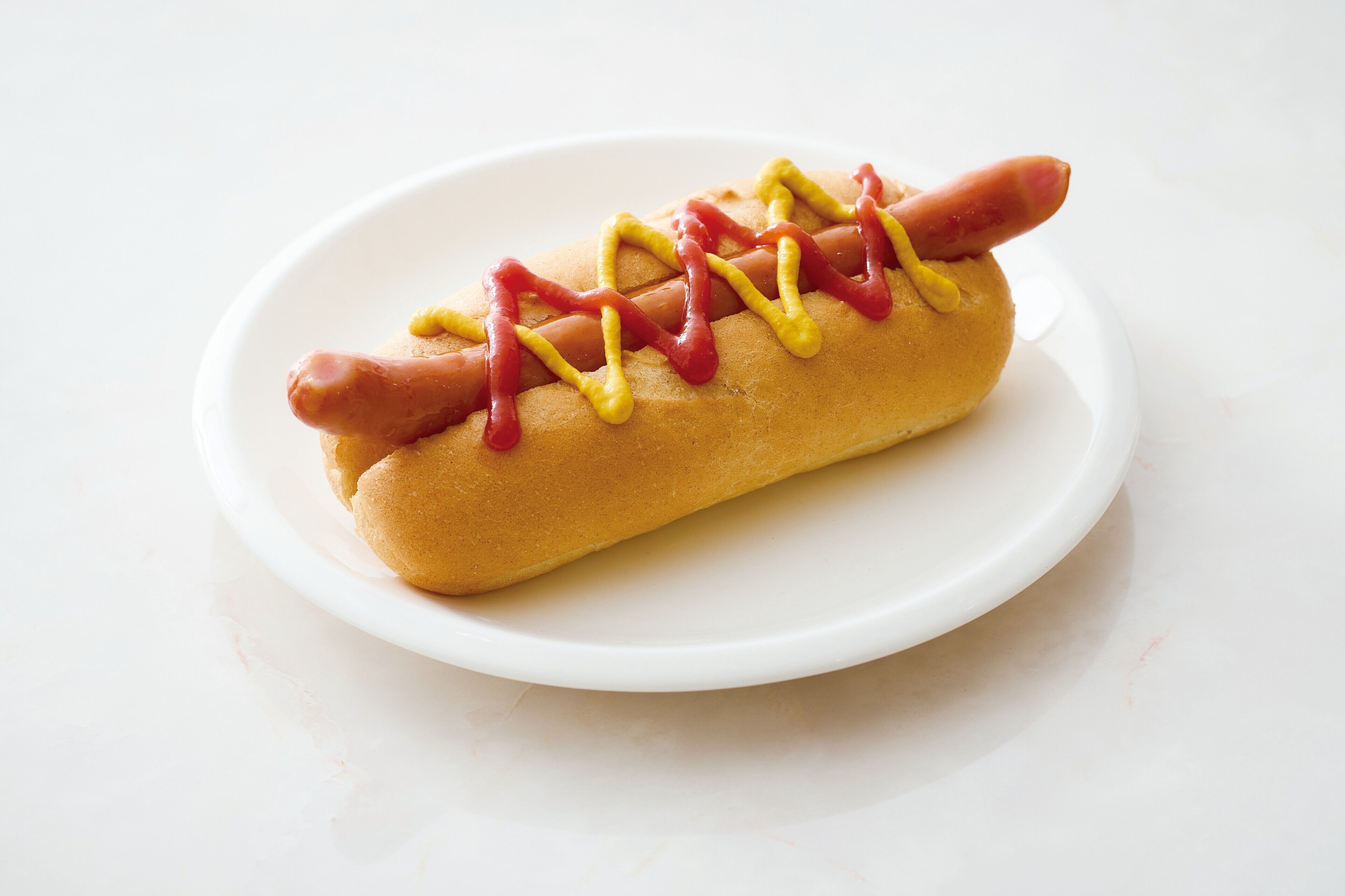 A hot dog with mustard and ketchup on a bun, placed on a white plate.