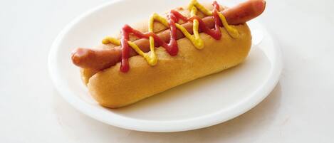 Un hot-dog garni de moutarde et de ketchup, servi dans un pain, et posé sur une assiette blanche.