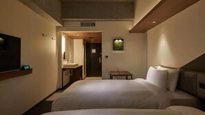 A hotel room with two beds, a TV, a small table, and a bathroom visible through an open door.