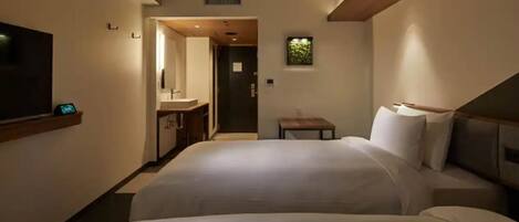 Habitación de hotel con dos camas, un televisor, una mesita y un baño visible a través de una puerta abierta.