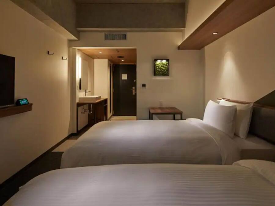 A hotel room with two beds, a TV, a small table, and a bathroom visible through an open door.