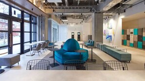 A modern interior with a blue sofa, tables, and chairs, large windows, and lockers.