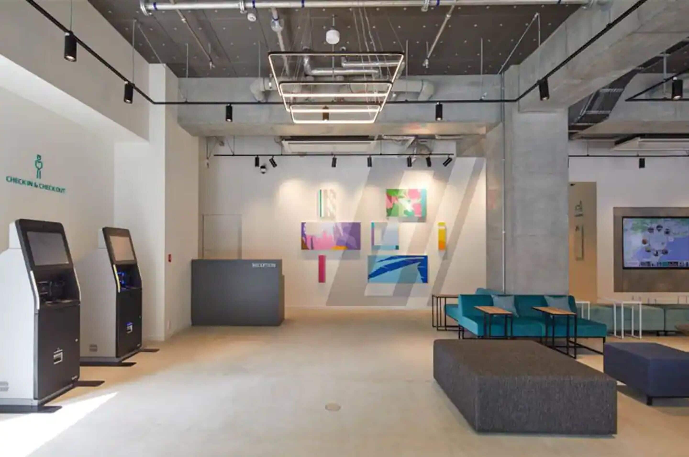 A modern reception area with a reception desk, self-service kiosks, and a seating area with a television screen.