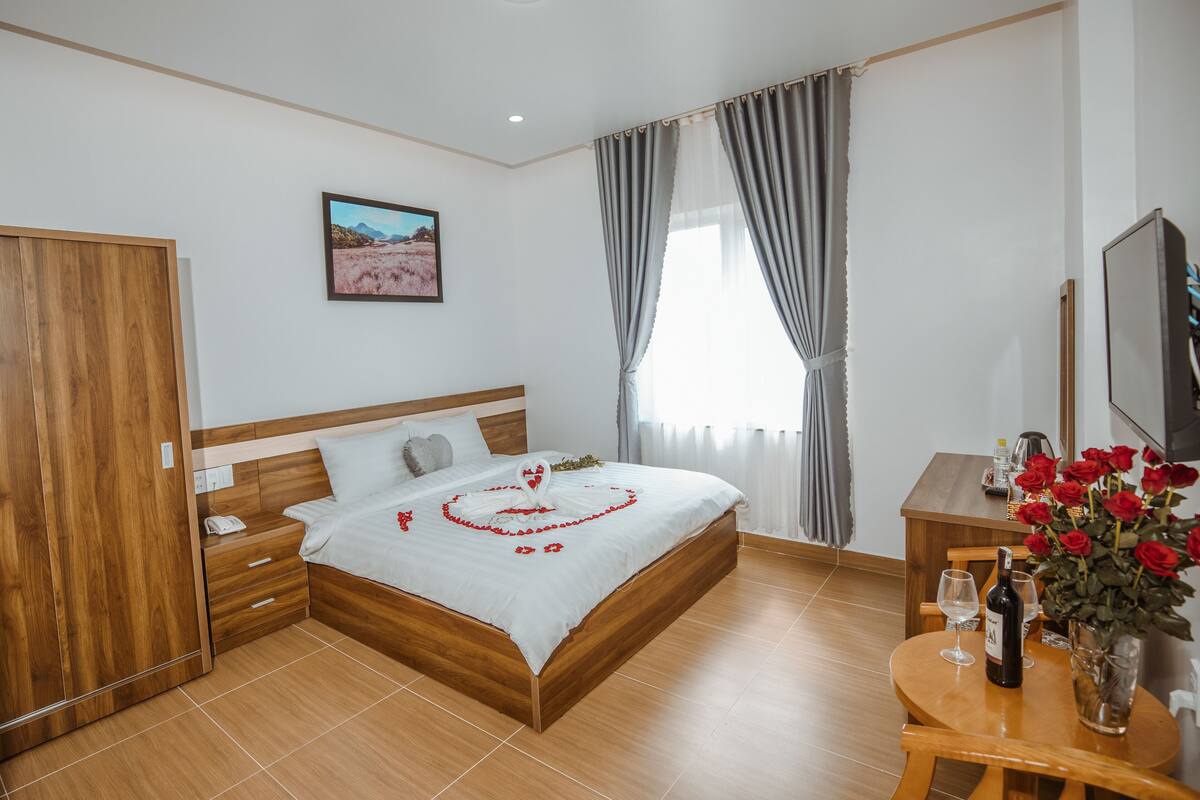 A neatly arranged bedroom with a wooden bed, a bedside table with a bottle and glasses, a wooden wardrobe, and a framed picture on the wall.