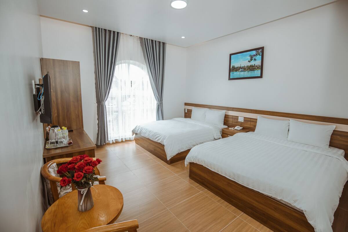 A hotel room with two beds, a wooden desk, a TV, and a painting on the wall.