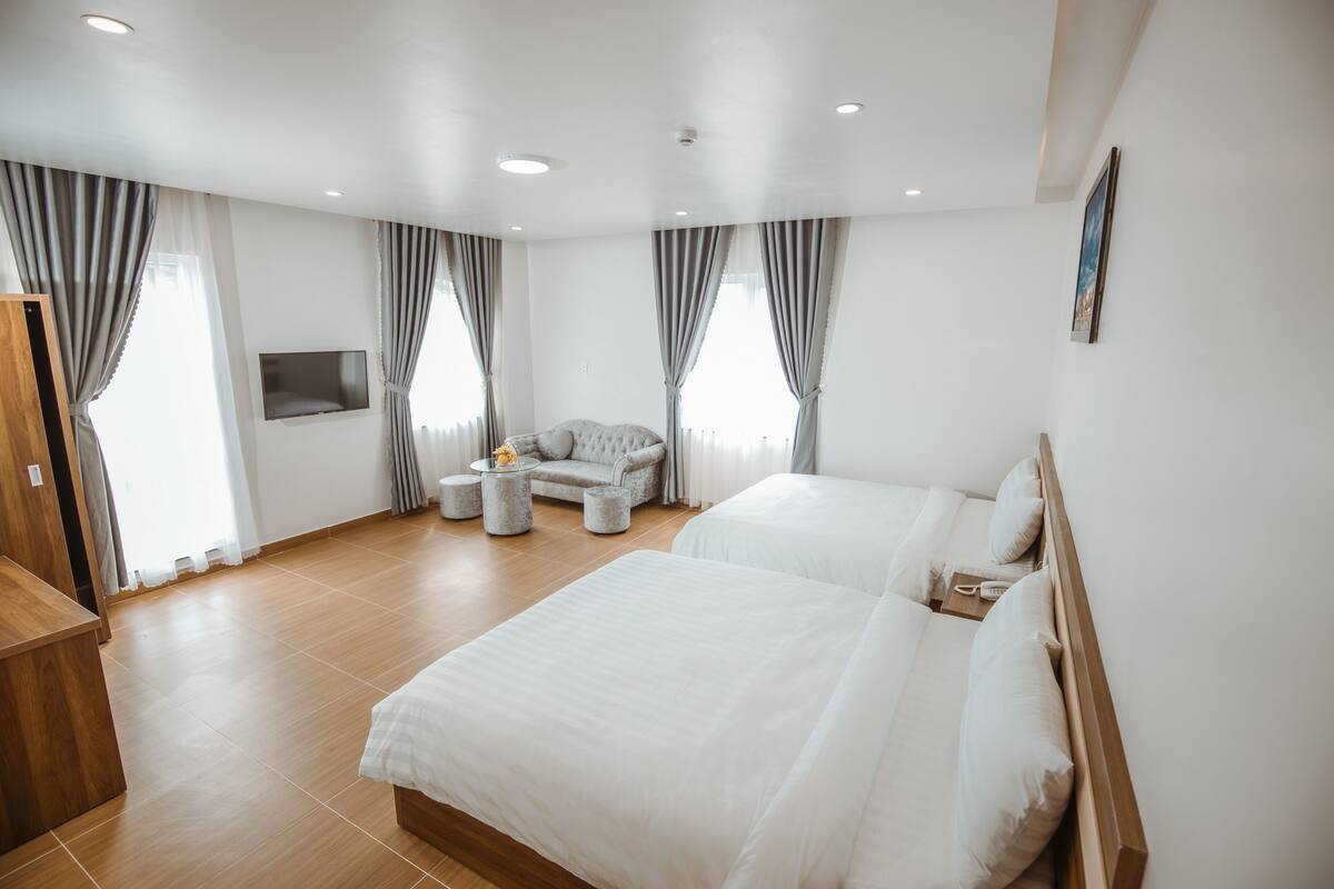 A modern hotel room with two beds, a sofa, a TV, and a wooden desk.
