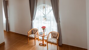 Une pièce avec deux chaises en bois, une petite table ronde et une fenêtre avec des rideaux.