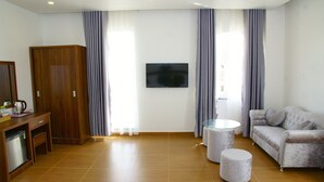 Une chambre d’hôtel avec une armoire en bois, un téléviseur fixé au mur, un canapé, une petite table ronde et une machine à café.