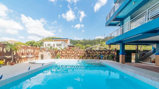 A swimming pool with a clear blue water surface, surrounded by a decorative stone wall and a blue building with a balcony. - RedDoorz Premium @ Casa Ghilda Resort Olongapo City (Olongapo)