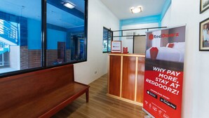 A hotel reception area with a wooden bench, a reception desk, and a poster advertising RedDoorz. - RedDoorz Premium @ Casa Ghilda Resort Olongapo City (Olongapo)