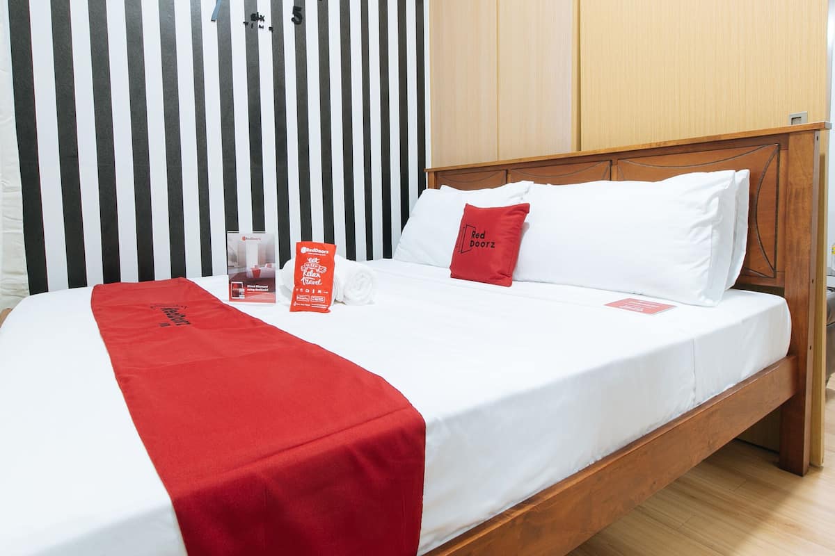 A neatly made bed with a white and red bedspread, a red pillow, and a red door sign on the nightstand.