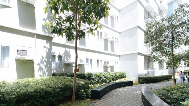 A modern building with a courtyard featuring a paved walkway, green hedges, and trees. - RedDoorz Premium @ SMDC Fairview 2 (Quezon City)
