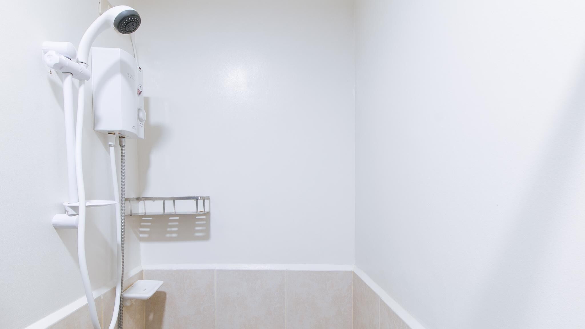 A shower with a handheld showerhead and a wall-mounted faucet, a small shelf, and a tiled floor.
