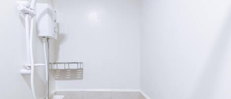 A shower with a handheld showerhead and a wall-mounted faucet, a small shelf, and a tiled floor.