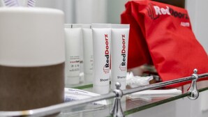 A bathroom counter with Red Doorz shower gel and shampoo, a brown container, and a red bag. - RedDoorz Plus @ Luzmin BH Lodging House (Oslob)