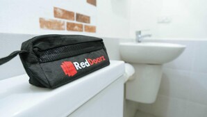 A black bag with "RedDoorz" logo on a white toilet in a bathroom with a sink and brown tiles on the wall. - RedDoorz Plus @ Luzmin BH Lodging House (Oslob)
