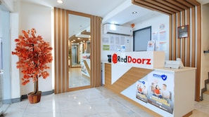 A reception area with a RedDoorz sign, a potted plant, and a mirror reflecting the interior. - RedDoorz Plus @ Jardin Suites Guadalupe Nuevo (Makati)