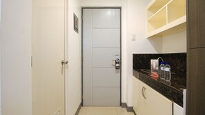 A narrow hallway with a white door, a water dispenser, and a countertop with a bottle of water. - RedDoorz Plus @ Jardin Suites Guadalupe Nuevo (Makati)