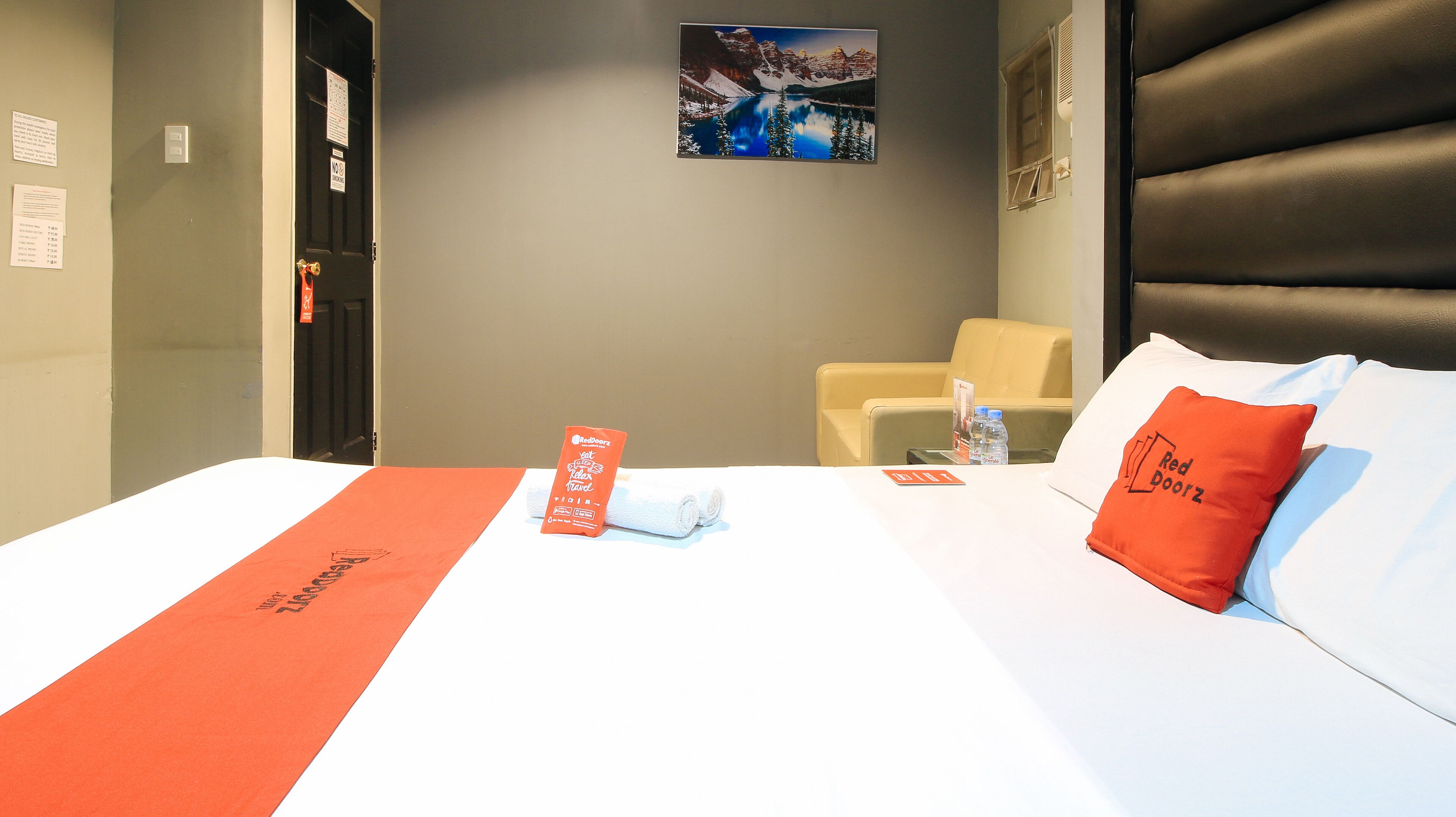 A hotel room with a bed, a chair, a desk, and a wall-mounted picture.