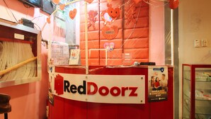 Un comptoir d’accueil RedDoorz aux couleurs rouge et blanc, avec un calendrier et un panneau indiquant que l’établissement offre un séjour sûr et confortable.