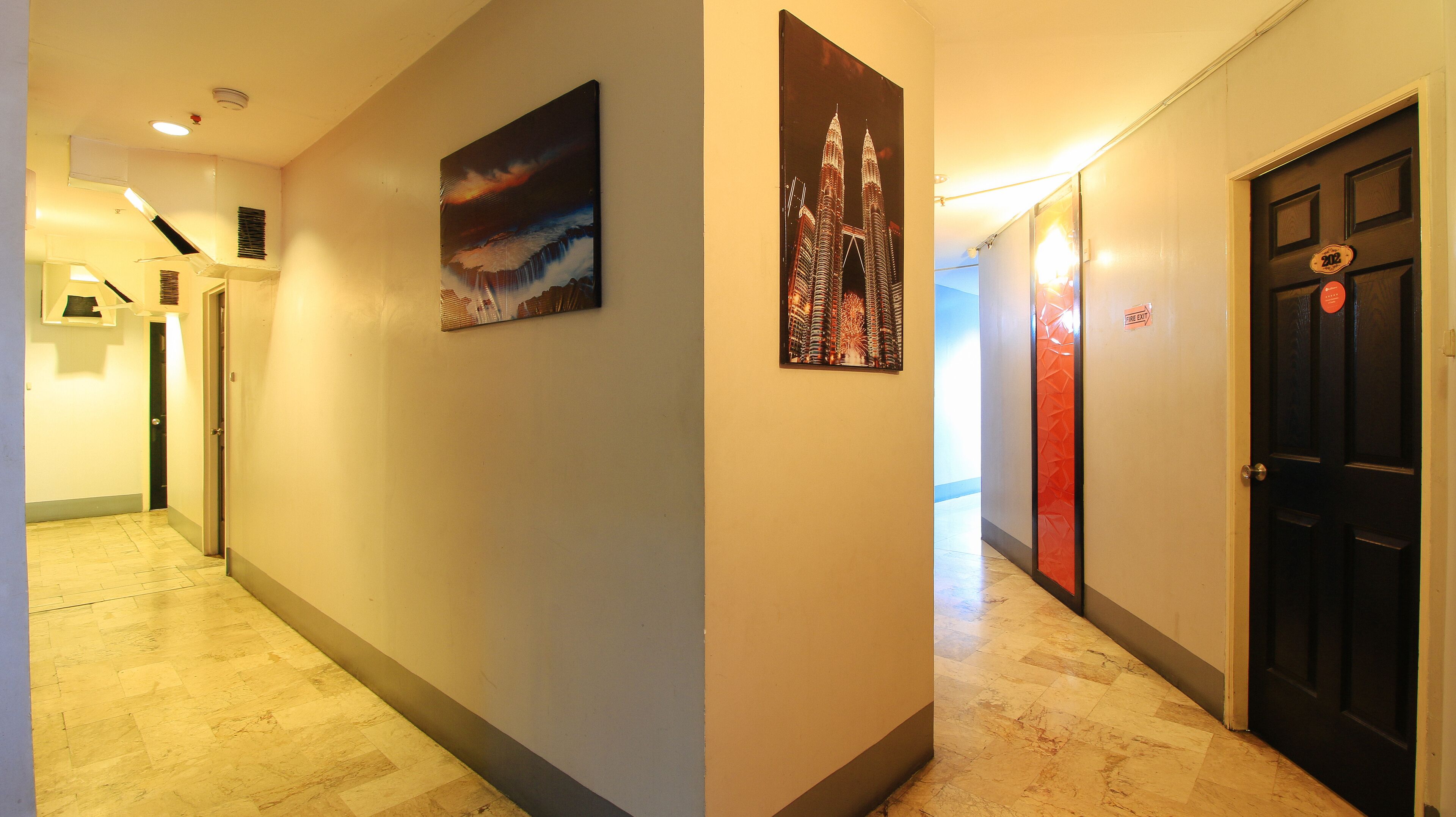 A hotel hallway with a tiled floor, a painting of a cityscape, and a door with a fire exit sign.