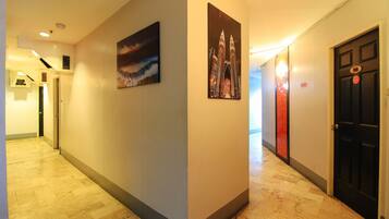 A hotel hallway with a tiled floor, a painting of a cityscape, and a door with a fire exit sign.