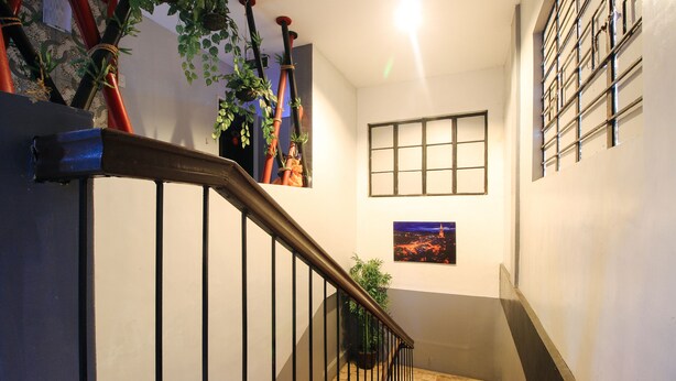 Un escalier avec une rampe métallique, une fenêtre à motifs géométriques et un tableau encadré accroché au mur.