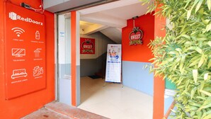 L’entrée d’un hôtel arborant la marque RedDoorz, une enseigne indiquant le « Sweet Hotel », et une liste des équipements proposés, notamment le Wi-Fi gratuit, de l’eau minérale, une télévision, une salle de bain, du linge de lit impeccable et d’autres commodités.