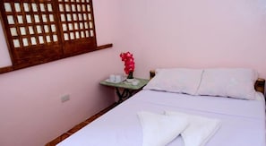 A bedroom with a bed, pillows, a nightstand with a red flower, and a window with a wooden lattice. - RedDoorz Plus @ Sla Divina Panglao Bohol (Panglao)