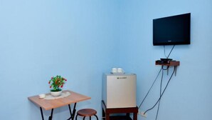 A small room with a single table, a chair, a potted plant, a refrigerator, and a mounted television. - RedDoorz Plus @ Sla Divina Panglao Bohol (Panglao)