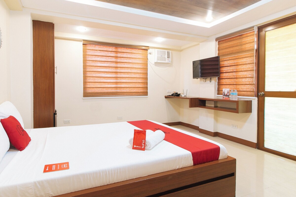 A hotel room with a bed, a desk, a television, and a window with blinds.