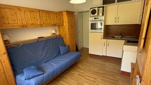 Un espacio habitable compacto con sofá, armarios de madera, una kitchenette y una lámpara de techo.
