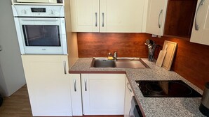 Cocina compacta con muebles blancos, horno microondas integrado, horno y encimera de granito.
